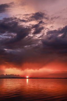 the sun is setting over the water and clouds