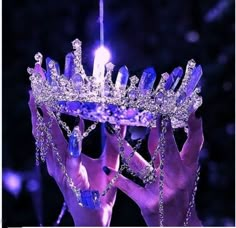 two hands holding up a tiara with purple lights on it in front of them