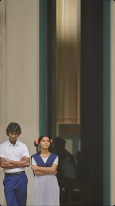 two people standing in front of a building with their arms crossed and looking at the camera