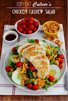 a white plate topped with chicken and salad next to two bowls of tomatoes, cucumbers and cherries