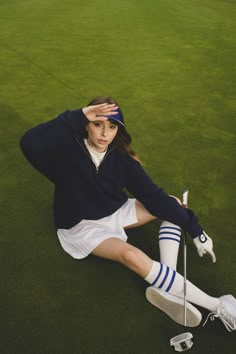 a woman sitting on top of a green field holding a golf club