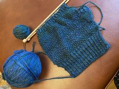 a blue knitted sweater sitting on top of a brown leather couch next to a ball of yarn