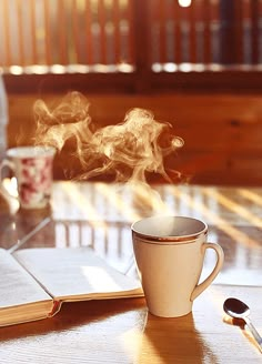 a cup of coffee sitting on top of a wooden table next to an open book