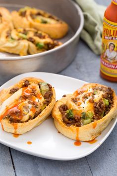 two mini pizzas sitting on top of a white plate next to a container of hot sauce