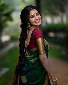 a woman with long hair wearing a green and red sari smiling at the camera