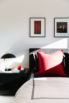 a bed with two red pillows and pictures on the wall above it in a bedroom