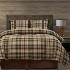 a bed with plaid comforter and pillows on top of it in front of a wooden wall