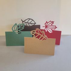 three folded cards with leaves on them sitting next to each other in front of a white wall