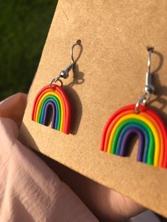 a pair of rainbow earrings is being held up by someone's hand in front of a piece of cardboard