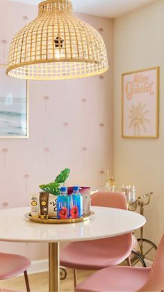 a white table topped with pink chairs next to a light hanging from a ceiling fixture