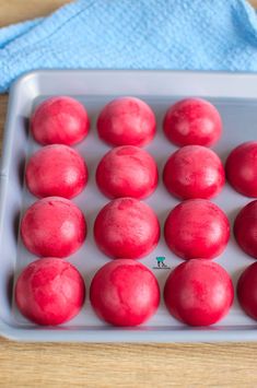 a pan filled with red doughnuts on top of a wooden table next to a blue towel