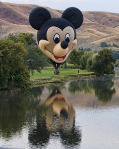 a large mickey mouse balloon floating over a lake