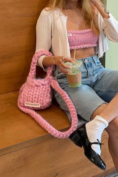 a woman sitting on a wooden bench holding a cup and a pink handbag in front of her face