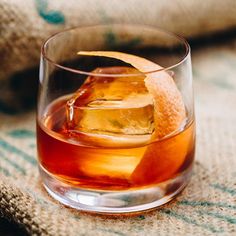 an old fashioned glass filled with ice and orange peel on top of a table cloth