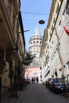 people are walking down an alley way with cars parked on both sides and a domed building in the background