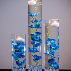 two tall vases with blue flowers and candles in them are sitting on a table