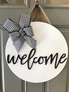 a welcome sign with a bow hanging from it's side on the front door