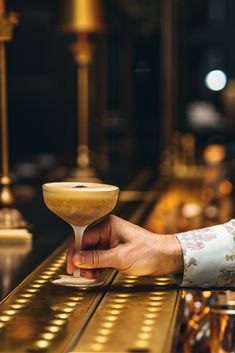 a person holding a drink in their hand on a bar with gold trimmings