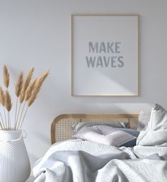 a bed with white sheets and pillows next to a framed print that says make waves