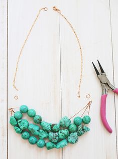 a pair of scissors and some turquoise beads on a white wooden table with pink handles