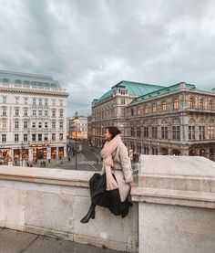 a woman sitting on the edge of a bridge looking down at buildings in the distance