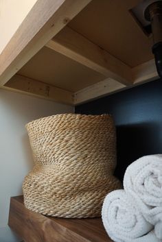 some white towels are on a shelf next to a large basket and light fixture in the corner