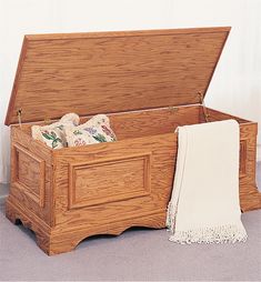 an open wooden chest sitting on the floor next to a white blanket and throw pillow