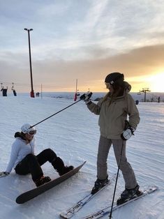 two people on skis in the snow with one person sitting down and another standing up