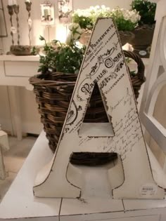 a wooden letter sitting on top of a table next to a basket filled with flowers