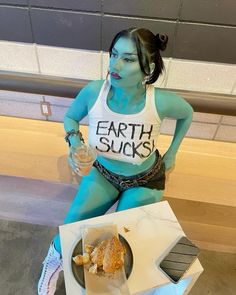 a woman with blue paint on her body sitting next to a box of doughnuts