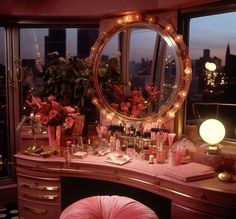 a vanity with flowers and candles on it in front of a large window at night