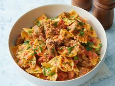 a white bowl filled with pasta and meat on top of a blue countertop next to a wooden container