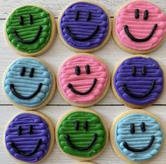 cookies decorated to look like smiley faces are arranged in rows on a white wooden surface