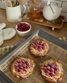 three pastries sitting on top of a table next to bowls of raspberries