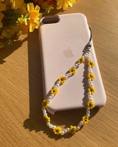 a white phone case with yellow and white beads attached to it on a table next to flowers