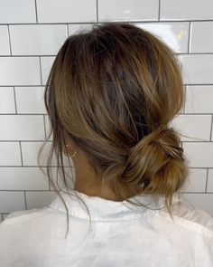 a woman with her hair in a low bun, standing against a white tiled wall