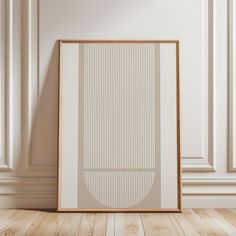 a white and gold framed art print on a wooden floor in front of a wall