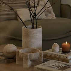 a table topped with books and a vase filled with flowers next to a candle on top of a wooden table