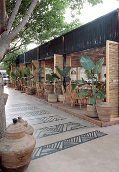 an outdoor patio with tables and chairs, potted plants on either side of the building