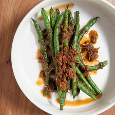 a white plate topped with green beans covered in sauce and brown stuff on top of it