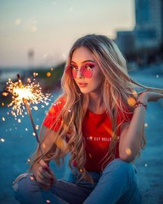 a woman sitting on the ground holding a sparkler in her hand and looking at the camera