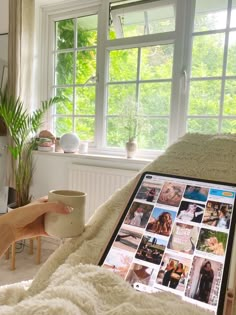 a woman sitting in bed with a laptop and coffee cup on her lap while looking at the screen