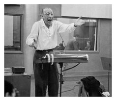 an old man standing in front of a microphone with his hands out to the side