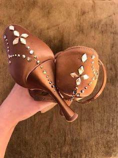 a woman's hand holding a pair of brown shoes with jewels on them,