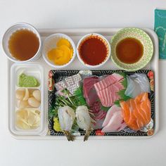 a tray with different types of sushi on it and sauces next to each other