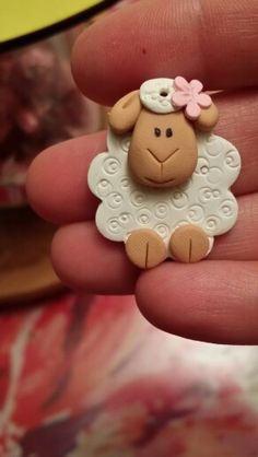 a small toy sheep with a pink flower on its head sitting in someone's hand