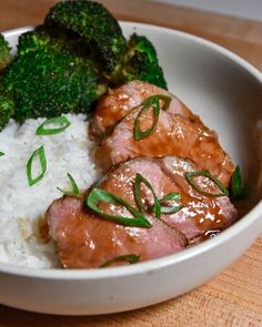 a white bowl filled with rice and meat covered in sauce next to broccoli