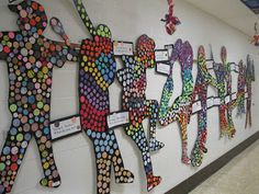 the wall is decorated with many different colored paper cutouts and people holding hands together