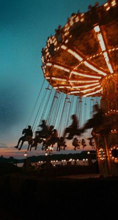 people are riding on a merry go round at night with the sun setting in the background