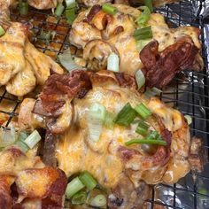 chicken wings covered in cheese, onions and green onions on a metal grill grate